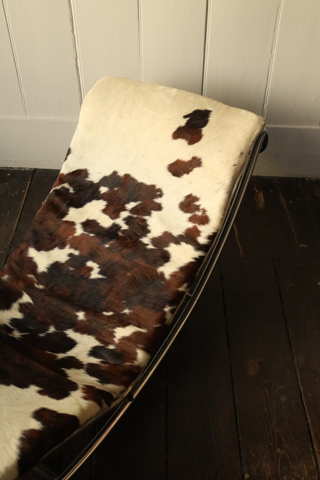 Angled view of the cowhide lounger chair, capturing the transition between hide sections and curvature of the frame.