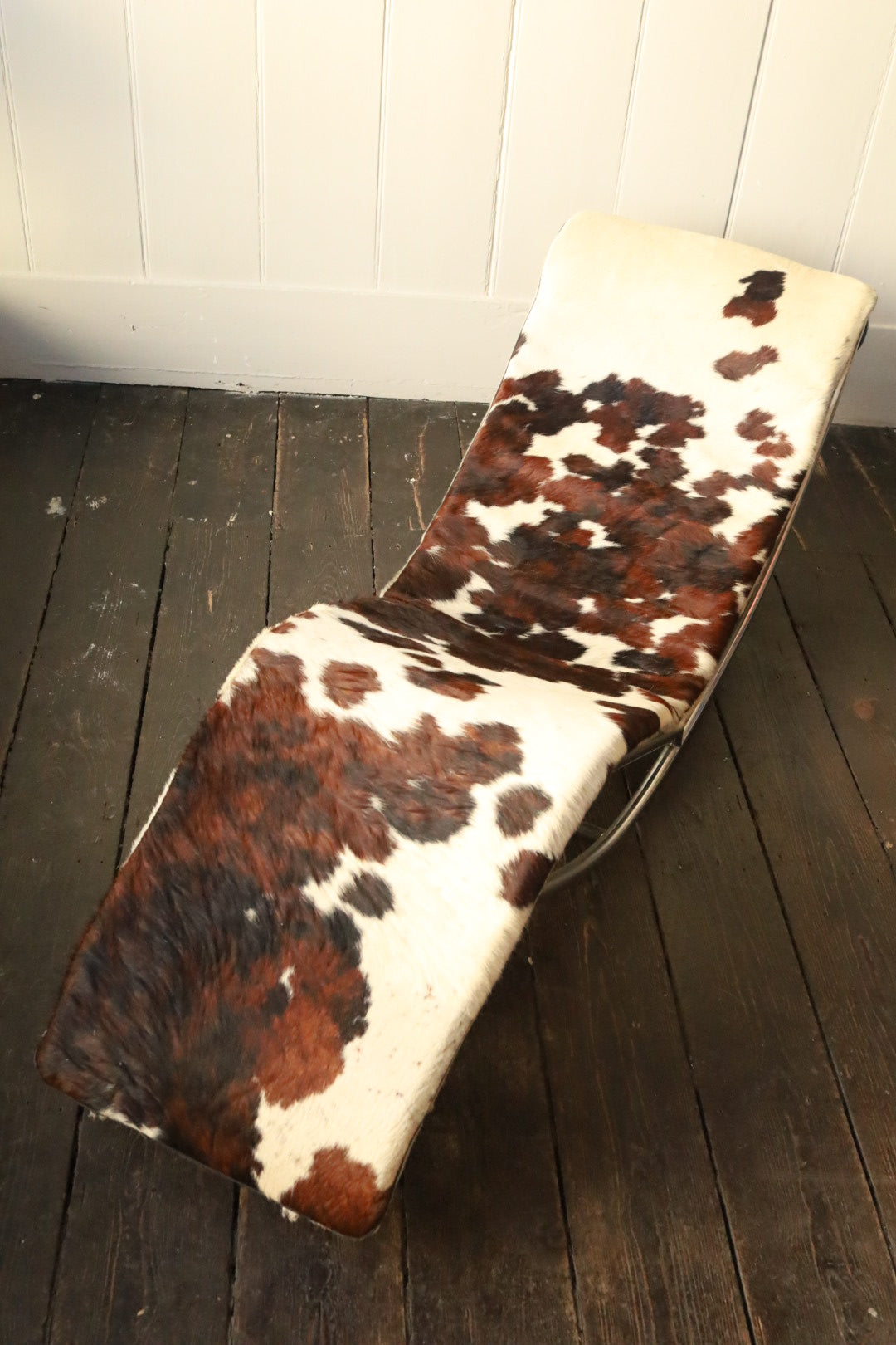 Front-facing image of the chair showcasing the full curved seat in brown and white cowhide and minimalist chrome base.