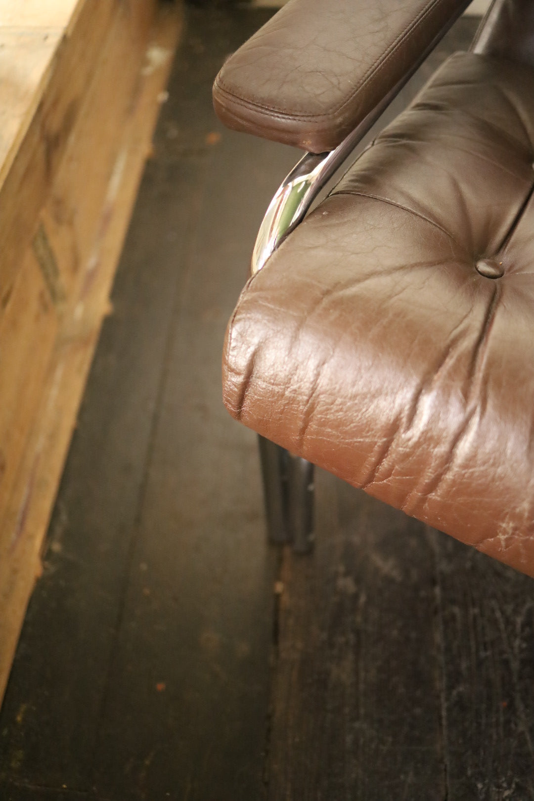 Close-up view of the left front corner of a Pieff Alpha sofa, focusing on the brown leather armrest, seat cushion with visible creases, and the chrome frame detail.