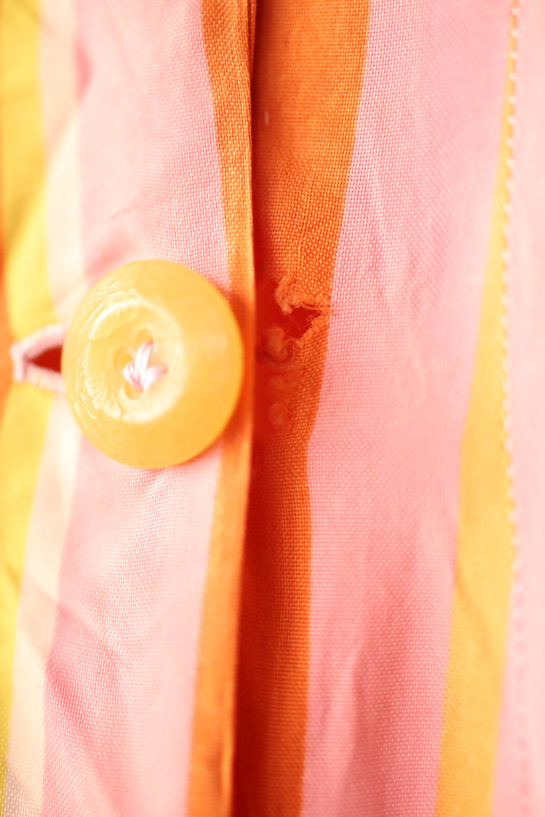 Close-up showing wear around the buttonhole area, with fraying of the fabric in orange and pink stripes.