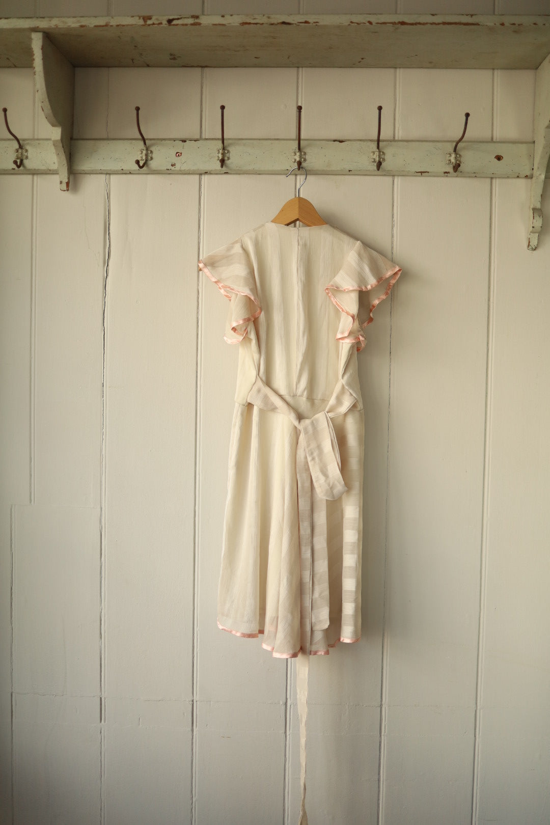 Rear view of the same cream dress showing flutter sleeves, concealed back zip, and long sash tie in matching fabric for a cinched waist.