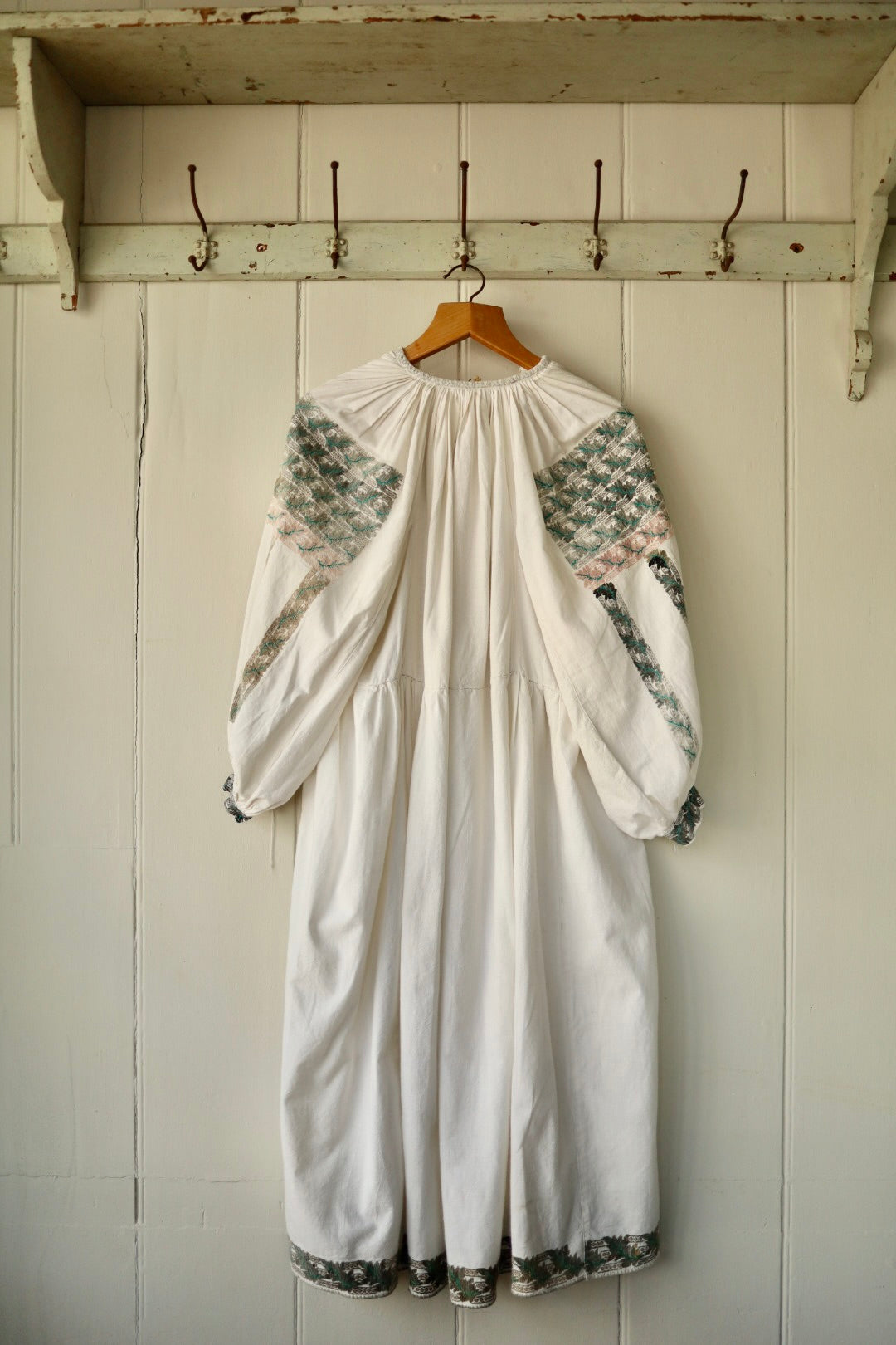 Back view of cream folk dress showing full sleeves with geometric embroidery in green and pink and a gathered upper back.