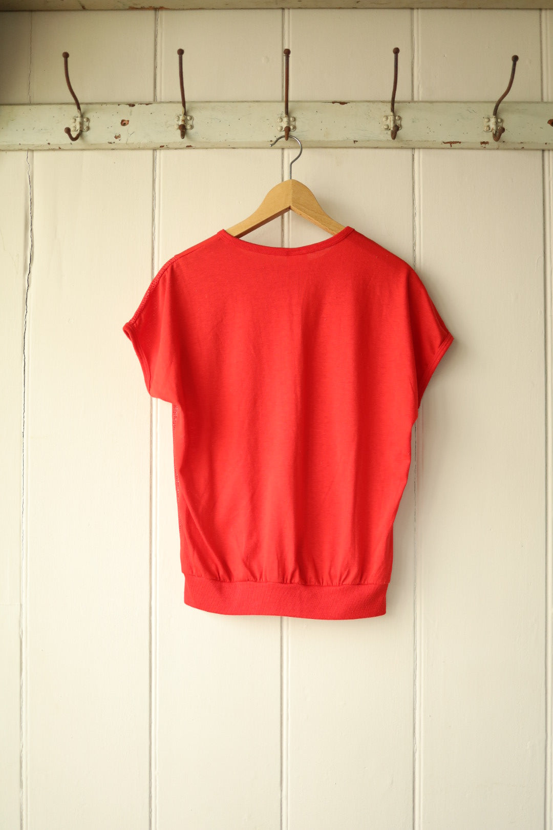 Back view of the same red Airtex tee against cream panelled wall