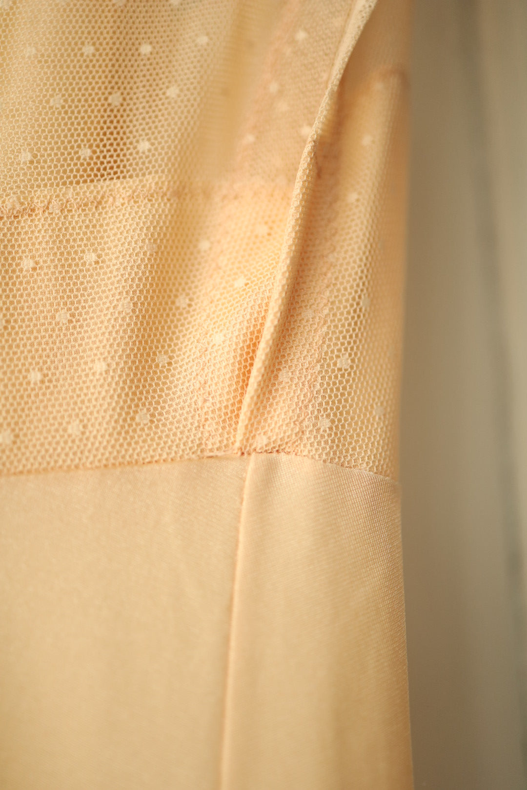 Detail of the nightdress bodice showing the scalloped seam where the polka dot mesh meets the peach fabric, with a V-neckline and softly gathered bust