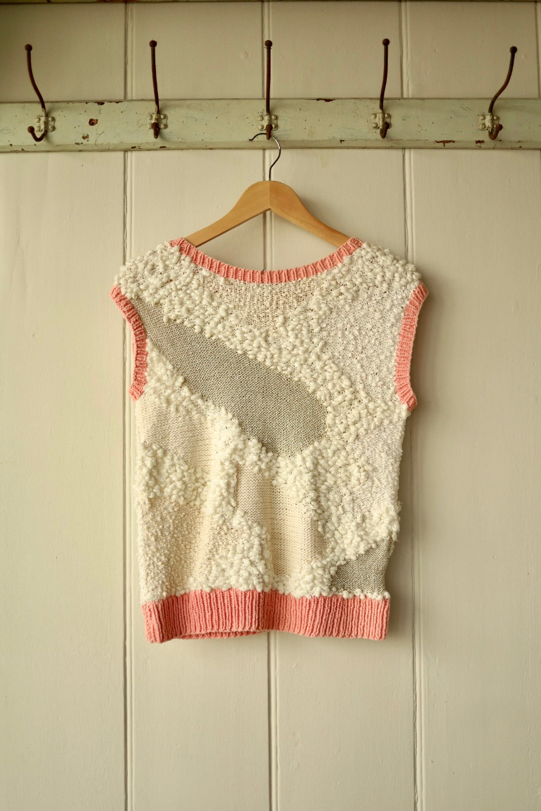 Back view of same knit vest showing patchwork of bobble and smooth knits with pink rib hem