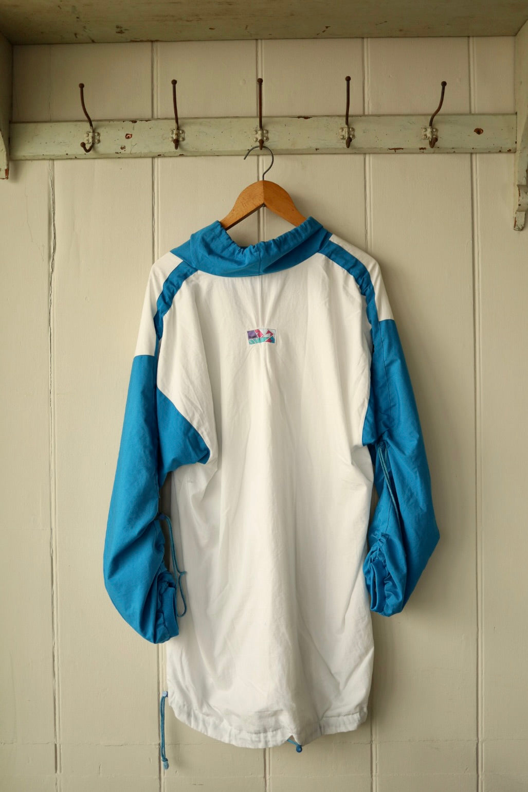 Back view showing white base, contrast sleeves and hood with small geometric patch at upper back