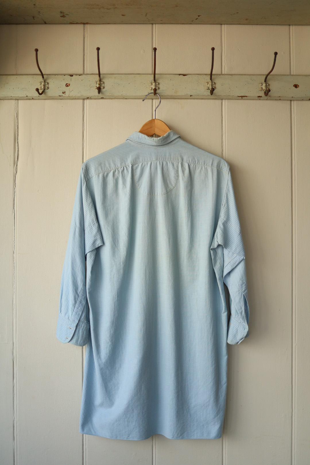 Back view of the same long pale blue shirt showing its relaxed cut and back yoke detail.