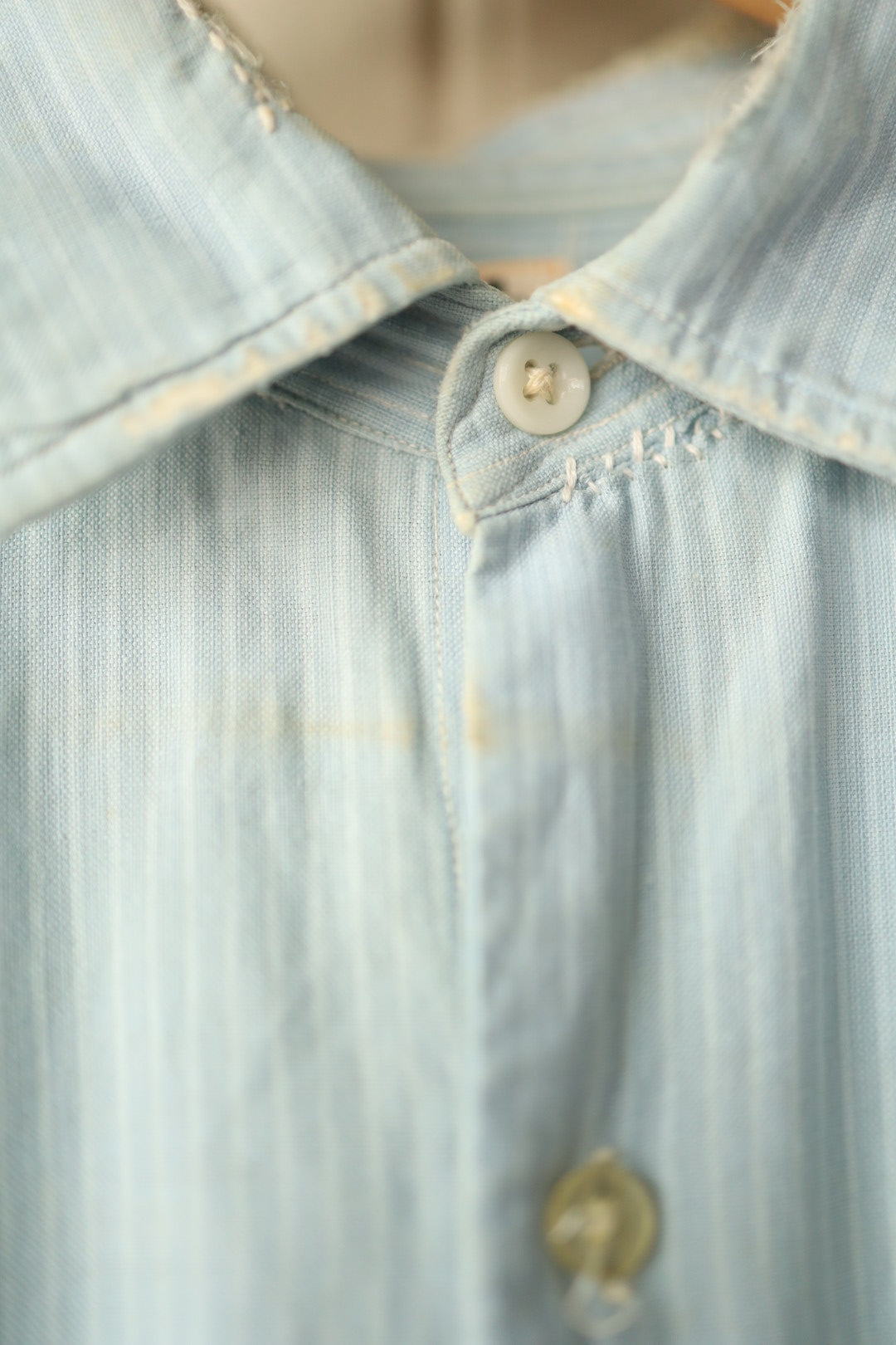 Detailed view of collar and top button showing small areas of discolouration and hand stitching near the neckline.
