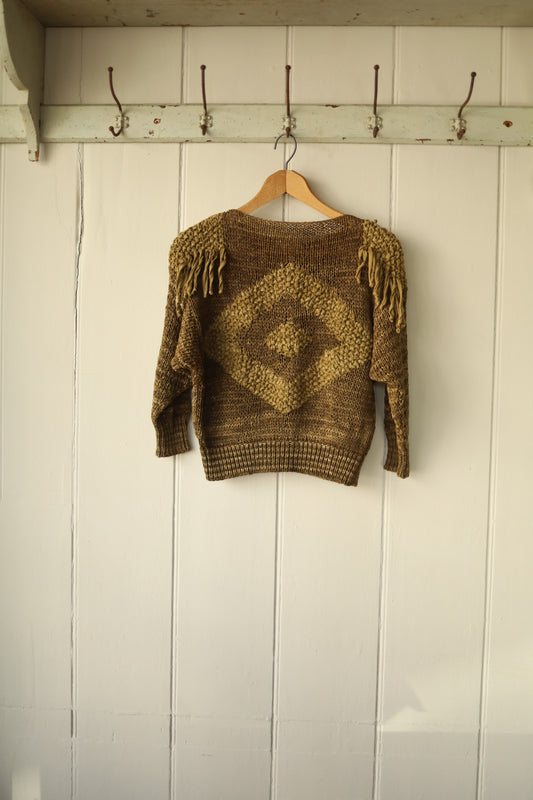 Flat lay of the jumper’s front, showcasing the symmetrical diamond intarsia motif and deep waistband.