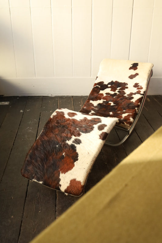 Cowhide and chrome lounger chair with smooth steel tubular frame and curved silhouette, upholstered in natural white and brown hide with visible grain.