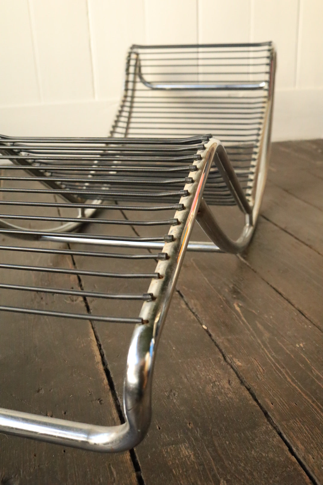 Close-up of one corner of the bare chrome lounger frame, showing spring attachments and metal wear.
