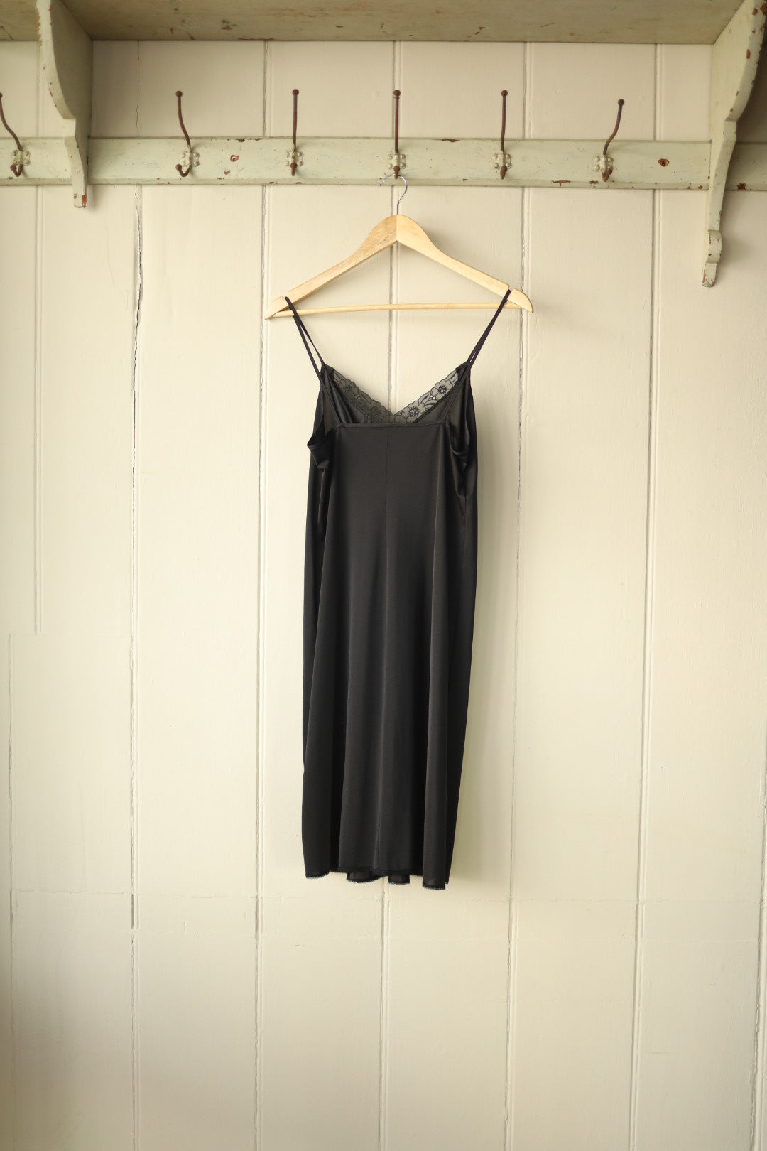 Back view of the same black vintage slip dress, showing simple silhouette and slim straps, displayed on hanger.