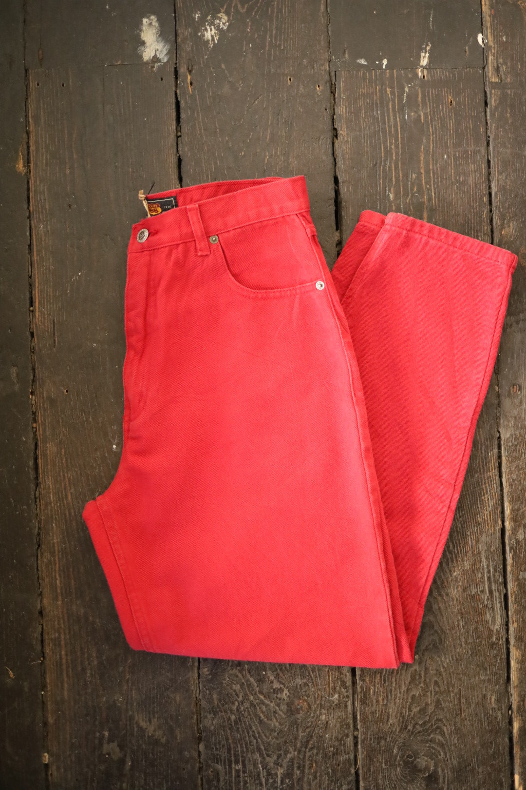Folded red Route 66 jeans displayed on a rustic wooden floor, highlighting the texture and colour of the denim.