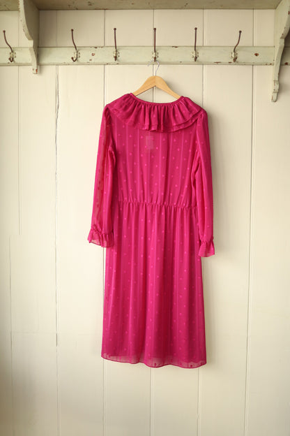 Back view of the raspberry pink sheer dress showing gathered waist and frill collar detail, displayed against a cream panelled wall.