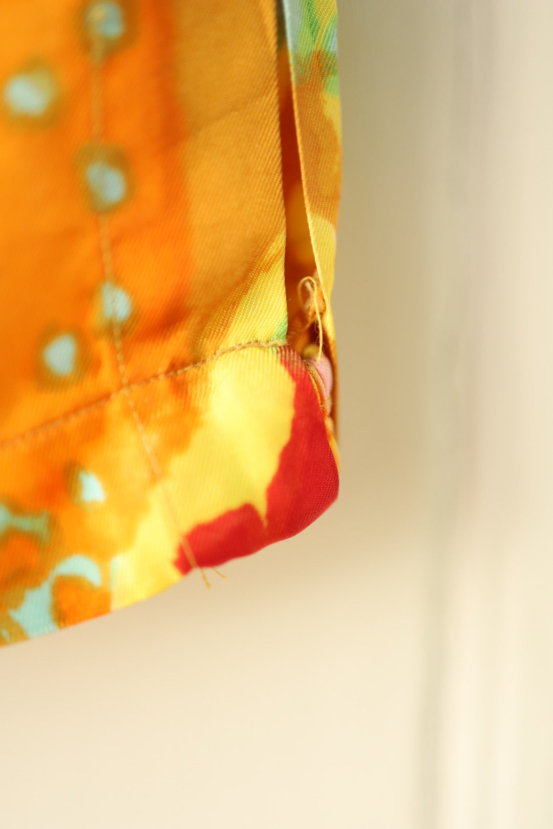 Close-up of the side hem showing a small area of loose stitching on the vibrant orange and red fabric.