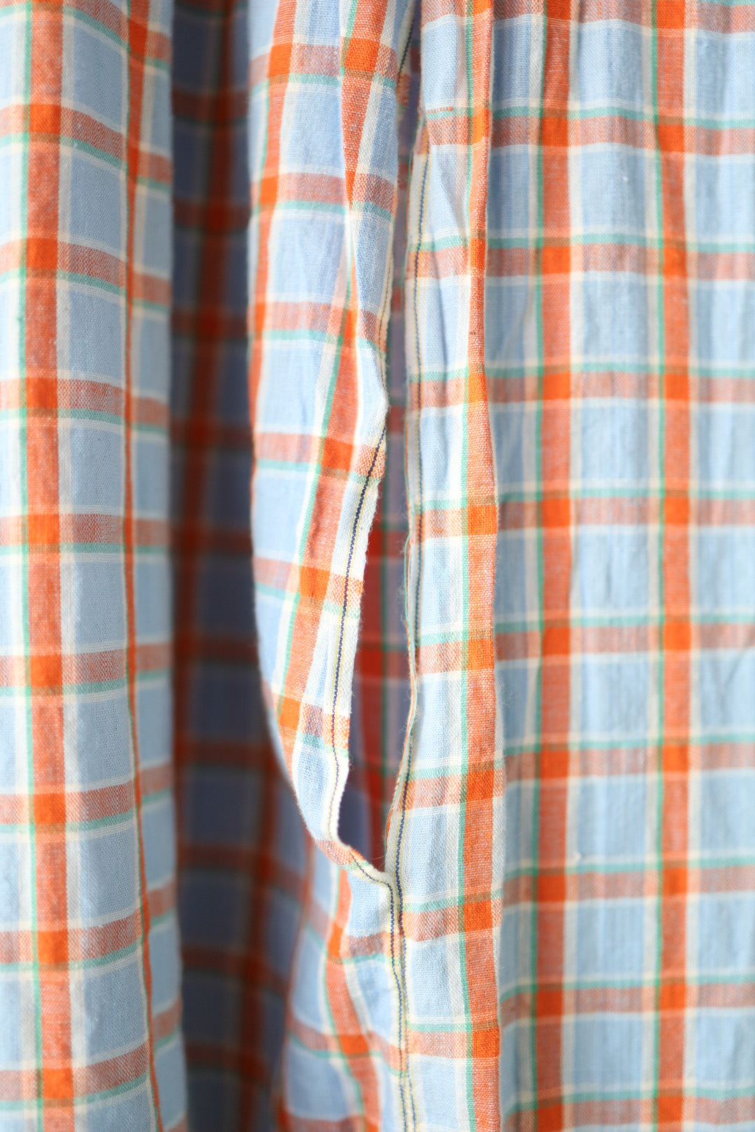 Close-up of the open pocket detail and fabric texture, highlighting the soft linen and orange plaid pattern with selvedge edge finish.