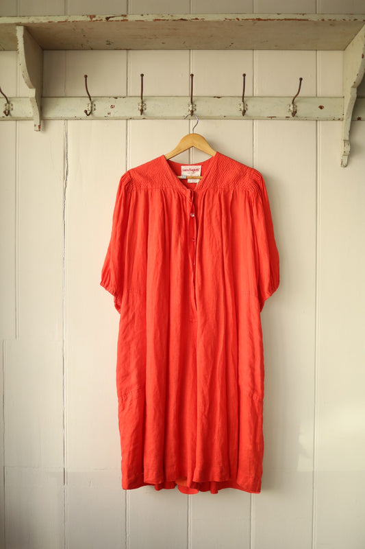 Front view of a loose-fit coral linen jumpsuit with stitched shoulder detailing and soft pleats.