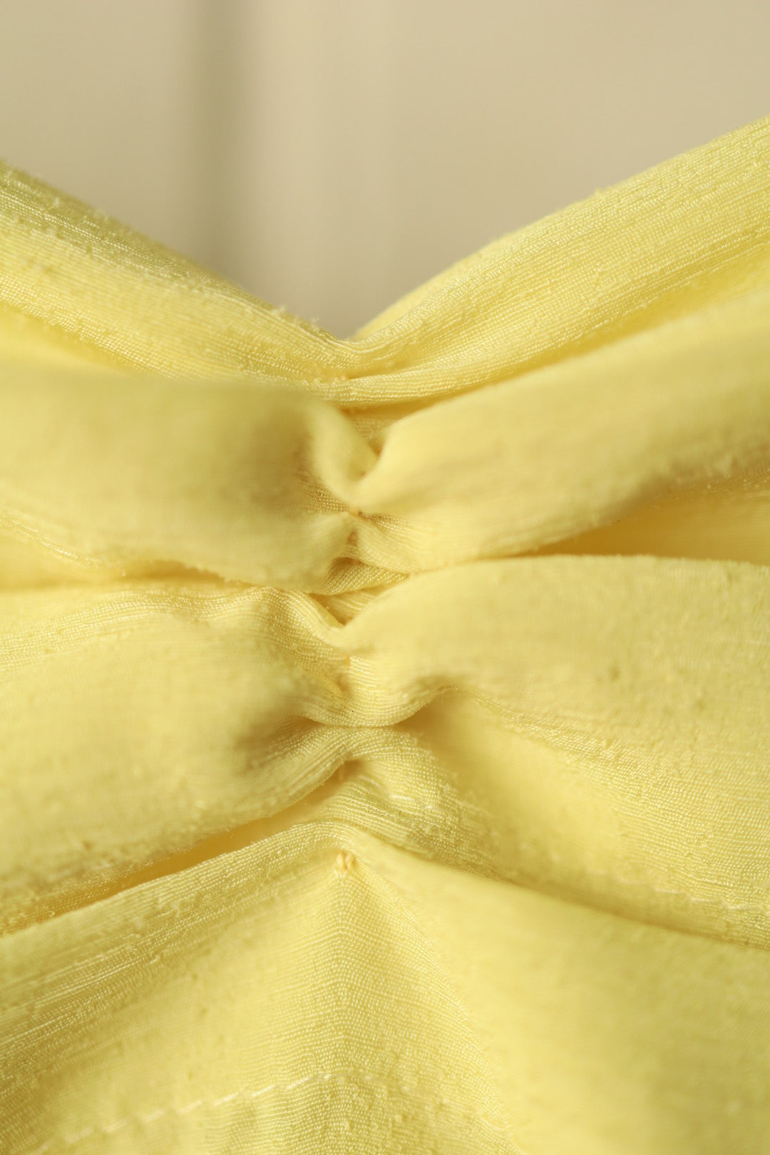 Extreme close-up of the pintuck pleats, showing the texture and stitching of the yellow fabric in fine detail.
