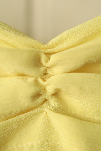 Extreme close-up of the pintuck pleats, showing the texture and stitching of the yellow fabric in fine detail.
