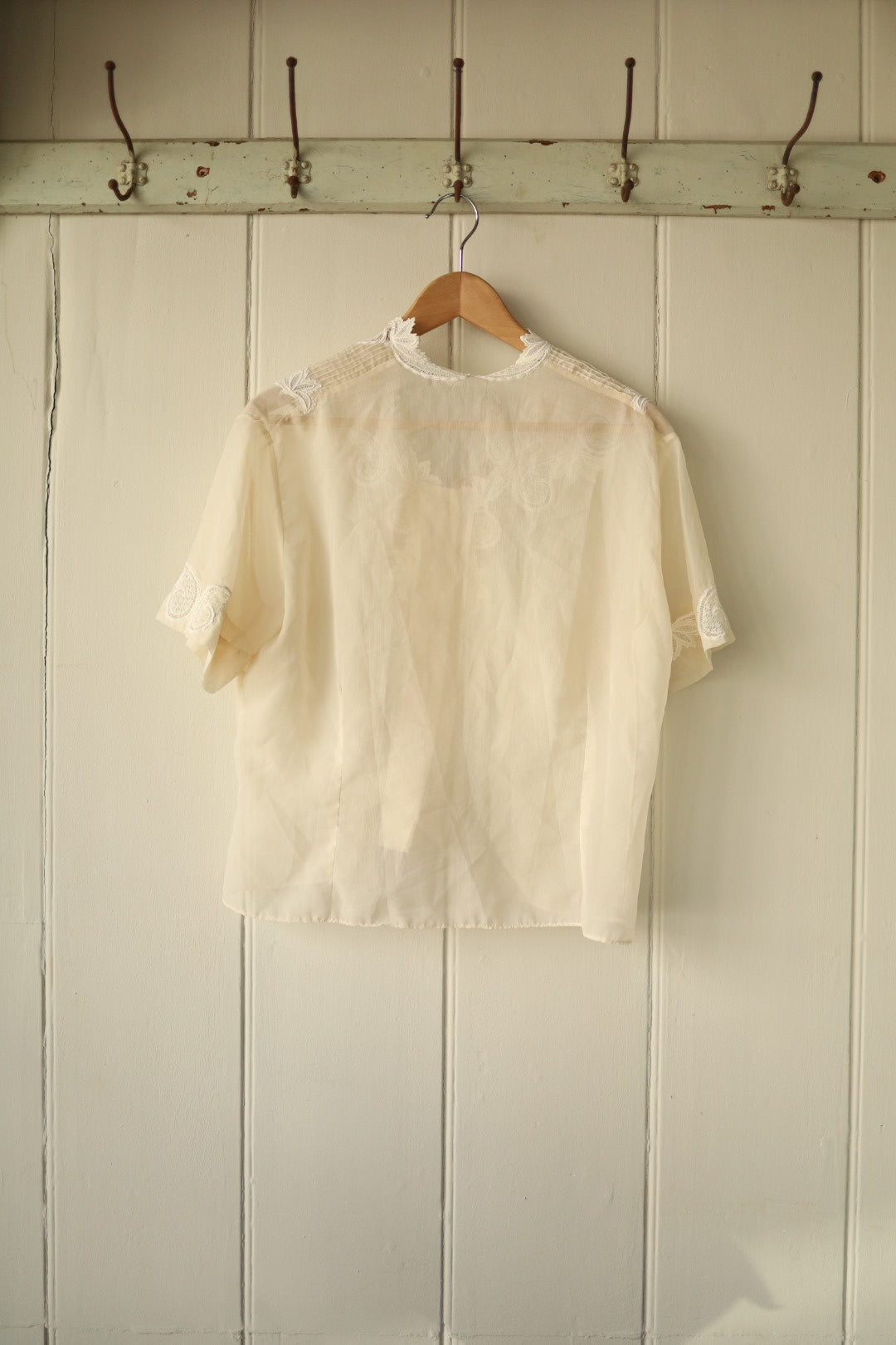 Back of the same sheer ivory blouse showing the cutwork embroidery details around the shoulder area, with a plain flowing back panel and short sleeves.
