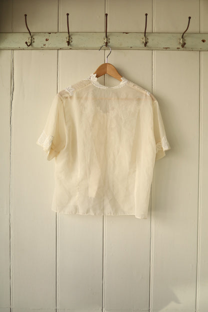 Back of the same sheer ivory blouse showing the cutwork embroidery details around the shoulder area, with a plain flowing back panel and short sleeves.
