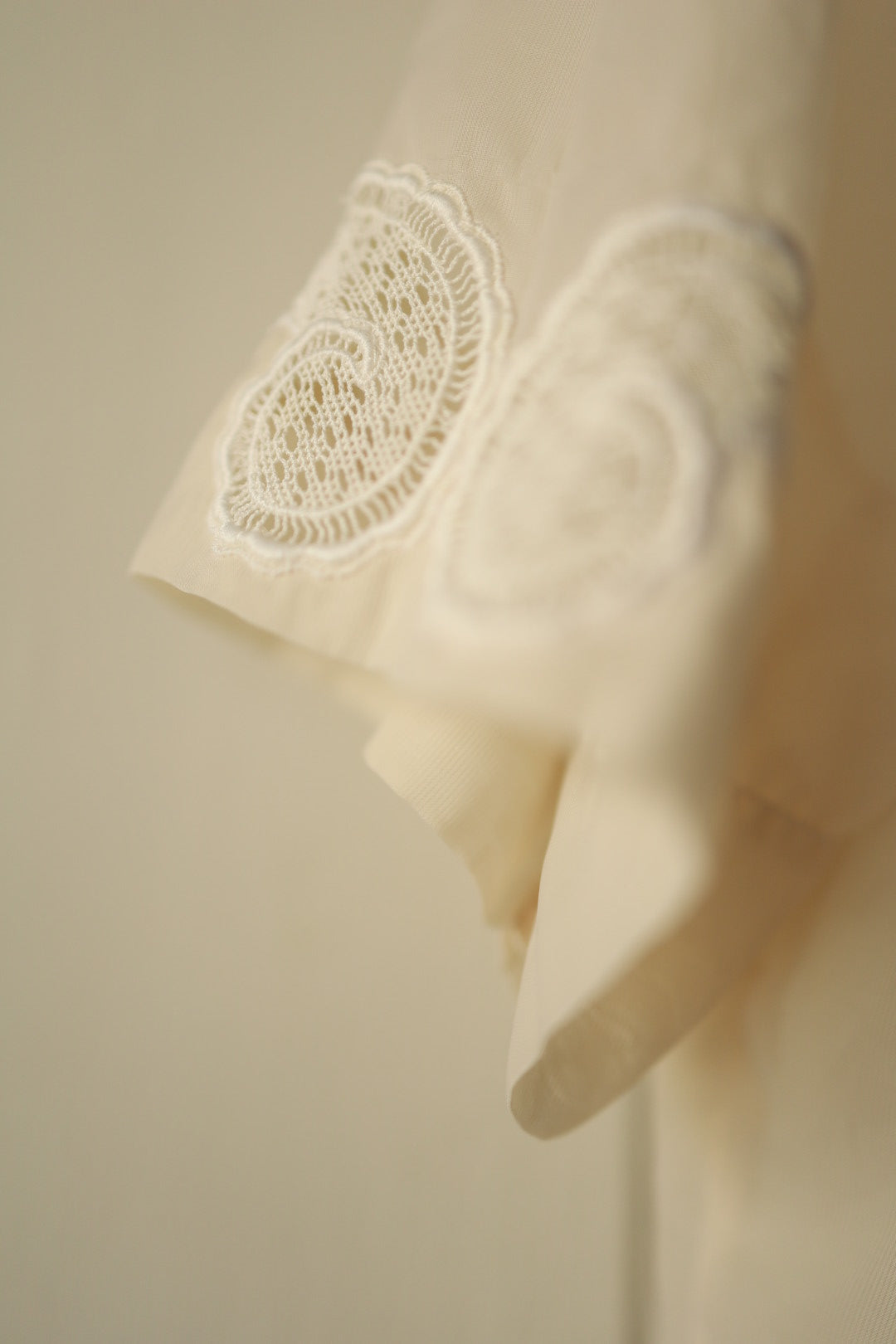 A close-up of the sleeve, capturing the intricate white embroidered lace design with fine floral and scroll motifs on the cuff.
