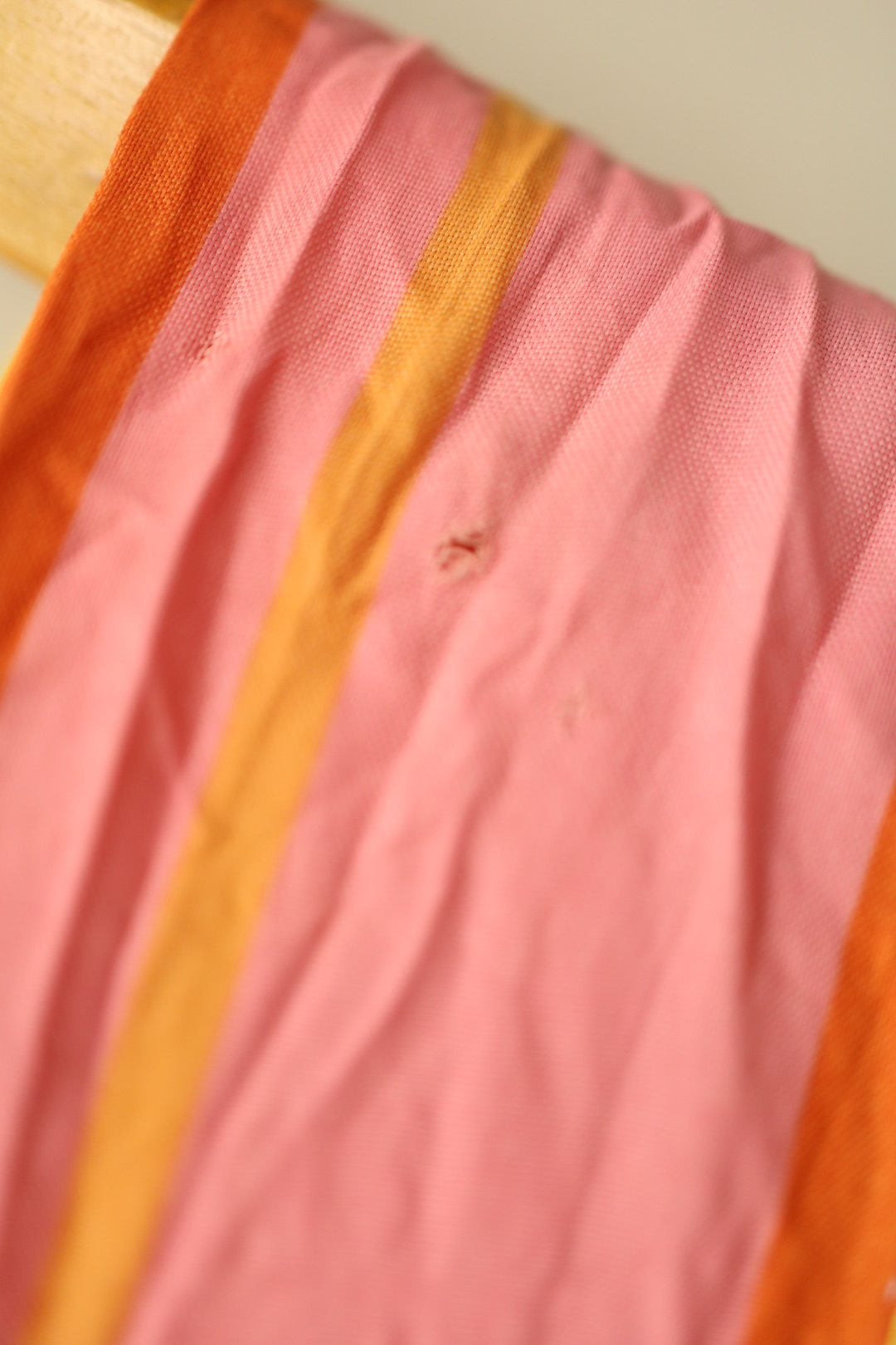 Close-up of a small hole and light snag on the shoulder area, highlighting fabric wear in the pink stripe.