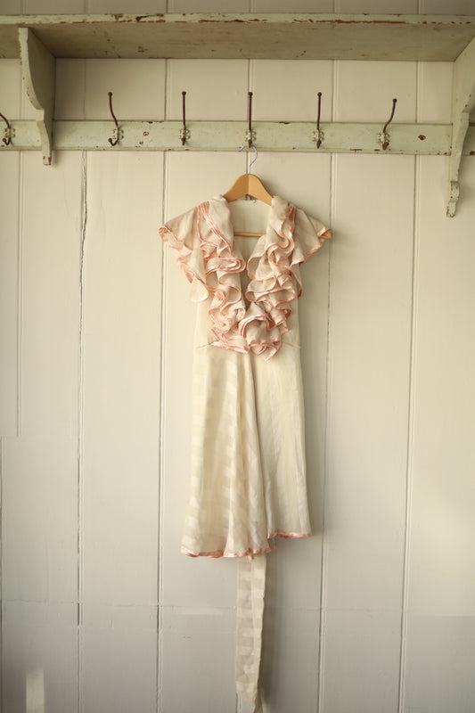 Cream mini dress with soft peach-pink ruffle trim, featuring dramatic layered ruffles down the front bodice and a fluid, striped skirt.