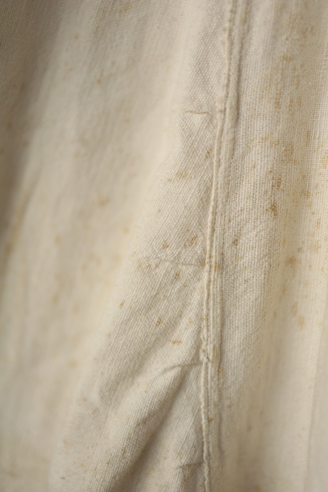 Focus on brown spotting and marks on the cream fabric, reflecting the dress’s vintage condition.