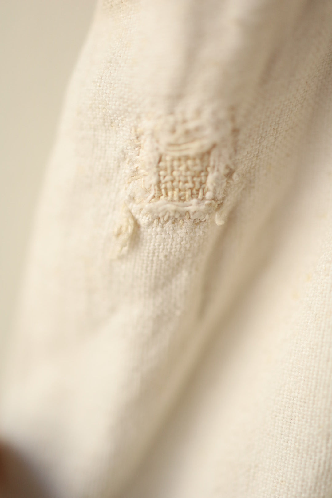 Macro photo of a square patch repair stitched into the fabric, showing the weave and hand-mending clearly.
