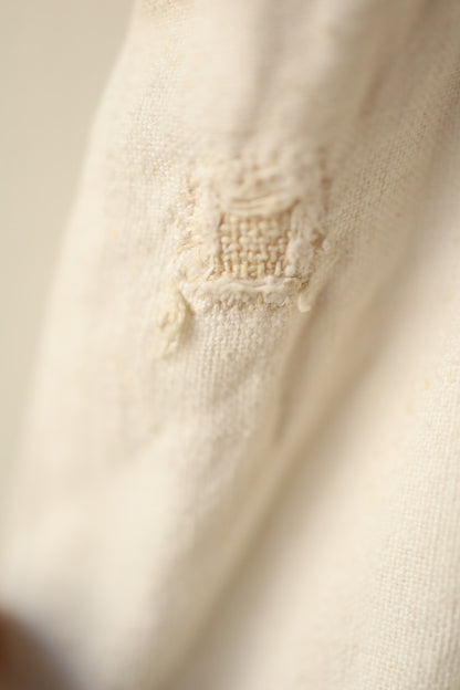 Macro photo of a square patch repair stitched into the fabric, showing the weave and hand-mending clearly.
