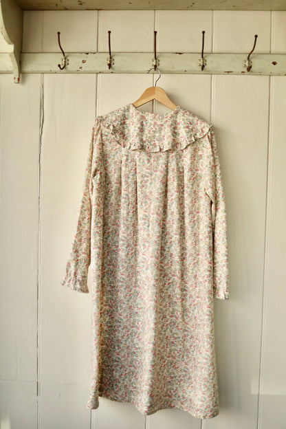 Back view of the same floral prairie collar smock dress showing its loose silhouette, delicate ruffle detail on the collar, and relaxed fit, hanging on a wooden hanger.