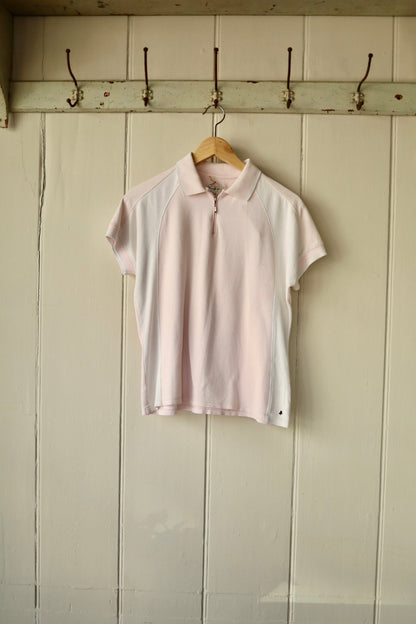 Vintage blush pink and white cotton tennis top with short raglan sleeves and a half-zip neckline, displayed on a wooden hanger against a cream panelled wall.