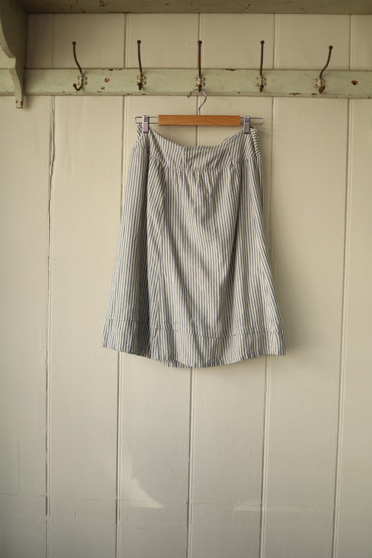 Front view of hickory striped antique cotton skirt hanging from wooden hanger against off-white panelled wall, showing A-line silhouette.