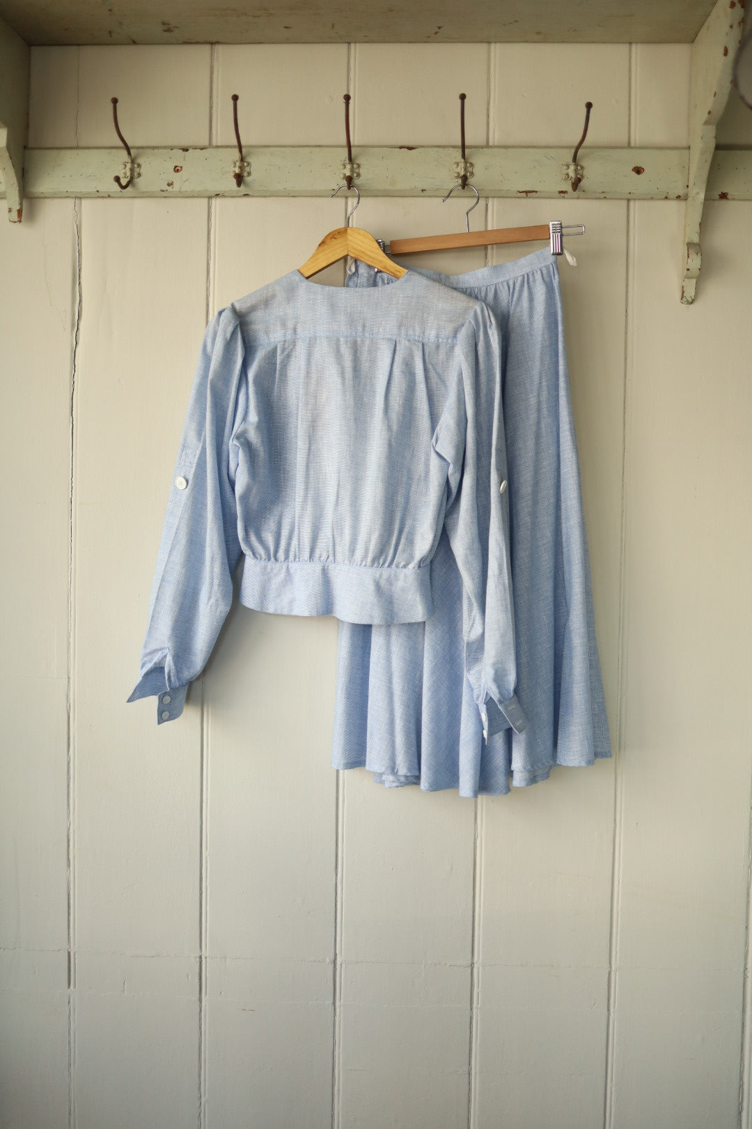 Rear view of the same Albert Nipon two-piece showing the simple gathered back and full skirt shape, hung on vintage hooks against a wooden backdrop.