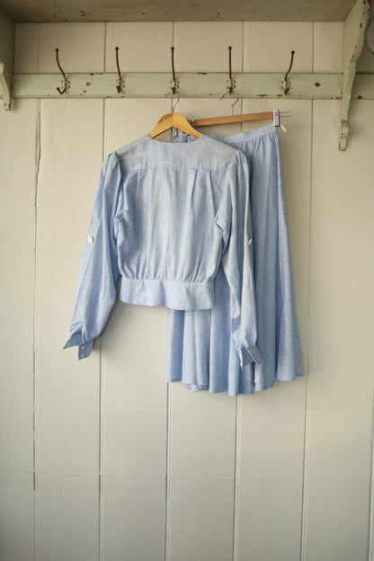 Rear view of the same Albert Nipon two-piece showing the simple gathered back and full skirt shape, hung on vintage hooks against a wooden backdrop.