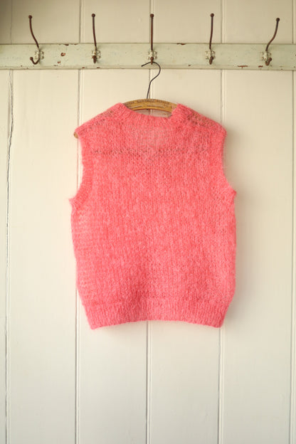 Front view of a hand-knitted bubblegum pink mohair vest hanging on a wooden hanger against a panelled wall.