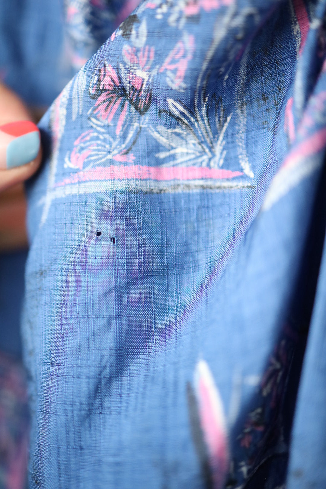 Macro photo of a small hole and light thinning in the fabric, set against printed floral design.