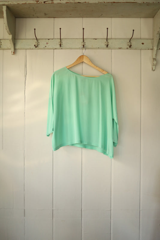 Missoni mint green silk batwing shirt with boat neckline, hanging on a wooden hanger against a white panelled wall