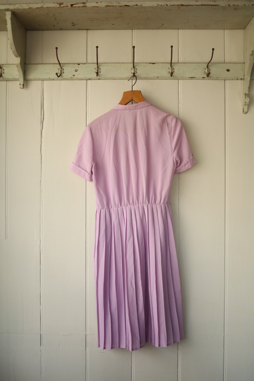 The back of the same dress showing the elasticated waistline and gently gathered pleats, displayed on a hanger against a neutral backdrop.