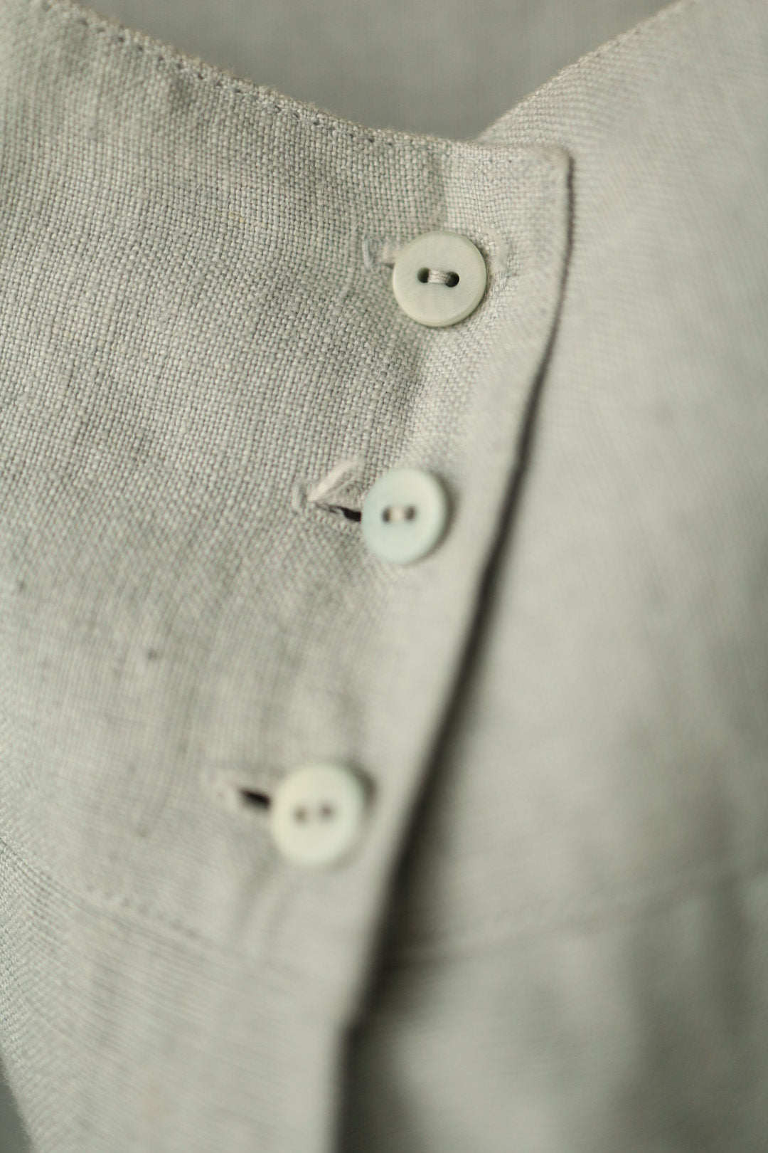 A close-up of the trousers’ high-waisted button fastening with three small round buttons in matching pale green.