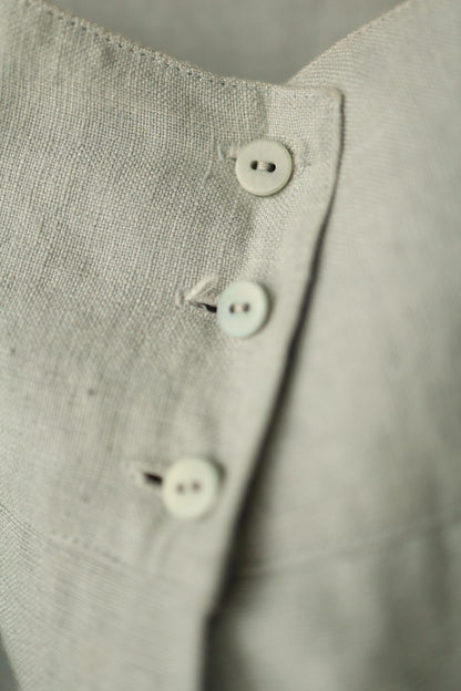 A close-up of the trousers’ high-waisted button fastening with three small round buttons in matching pale green.