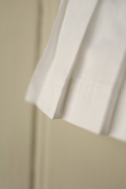 Detailed close-up showing the pleated hem and crisp cotton texture of the white tennis skirt.