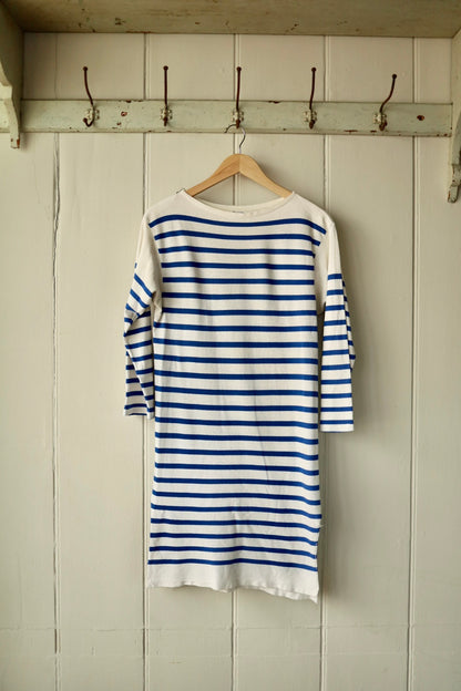 Back view of a vintage Orcival Breton dress in cream with classic cobalt blue stripes, displayed on a wooden hanger against a painted wooden wall with iron hooks.