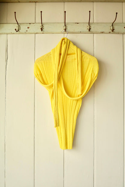 Back view of the yellow ribbed stretch top, with its elongated sleeves draped over the shoulders, showing the sculptural knit and form-fitting silhouette.