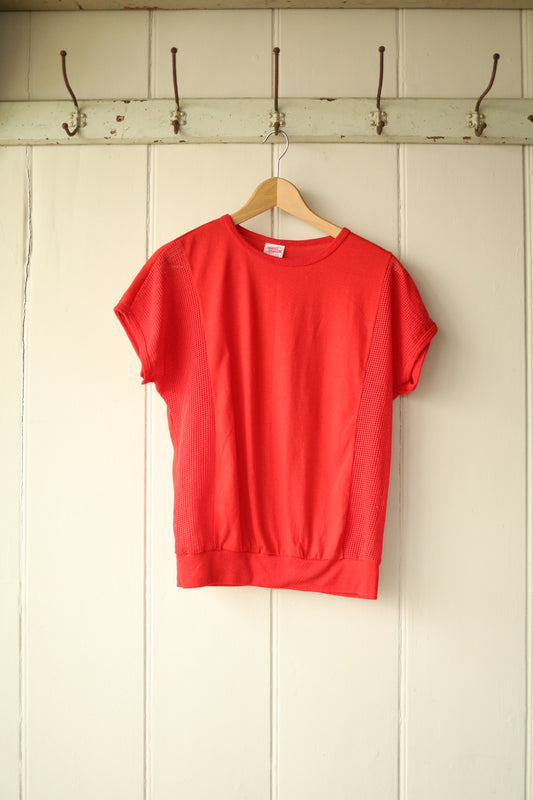 Front view of vintage red 1980s Airtex tee with mesh side panels, hanging on a wooden hanger