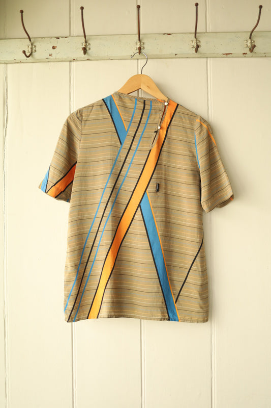 Front view of a vintage silk shell top featuring bold geometric stripes in orange, blue, and black across a beige pinstripe background, with a side button fastening at the shoulder.