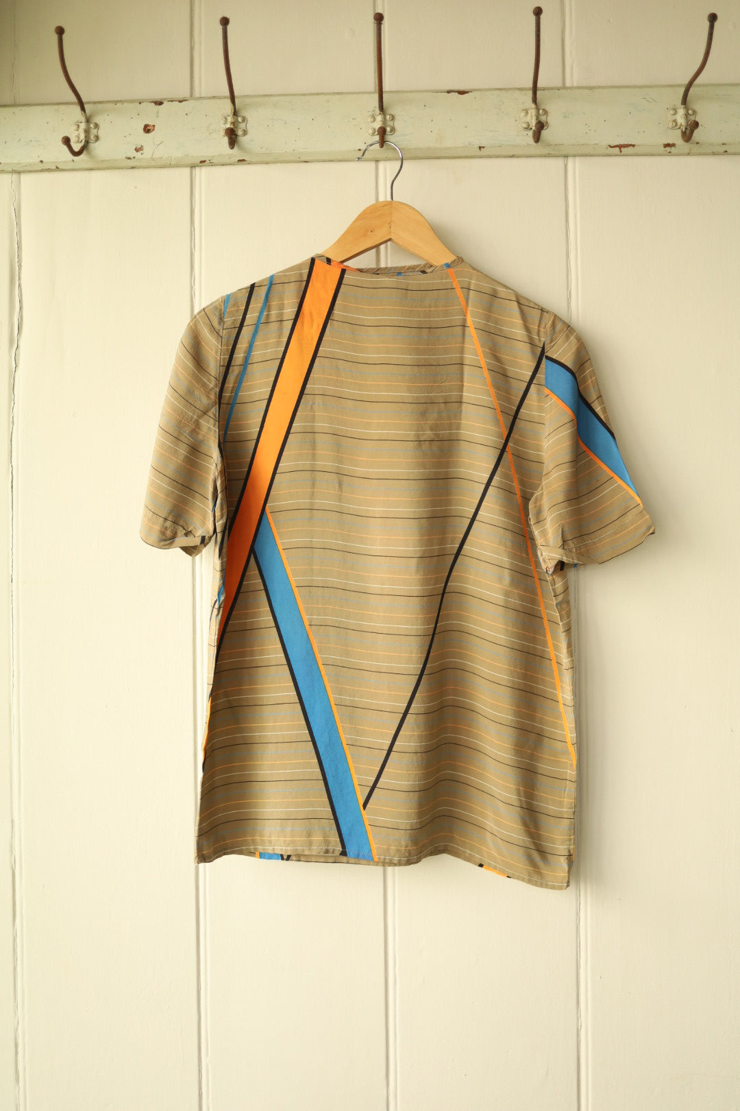 Back view of a short-sleeved vintage silk shell top with a beige base and diagonal orange, blue, and black stripes.