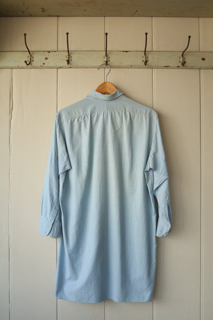 Back view of the same long pale blue shirt showing its relaxed cut and back yoke detail.
