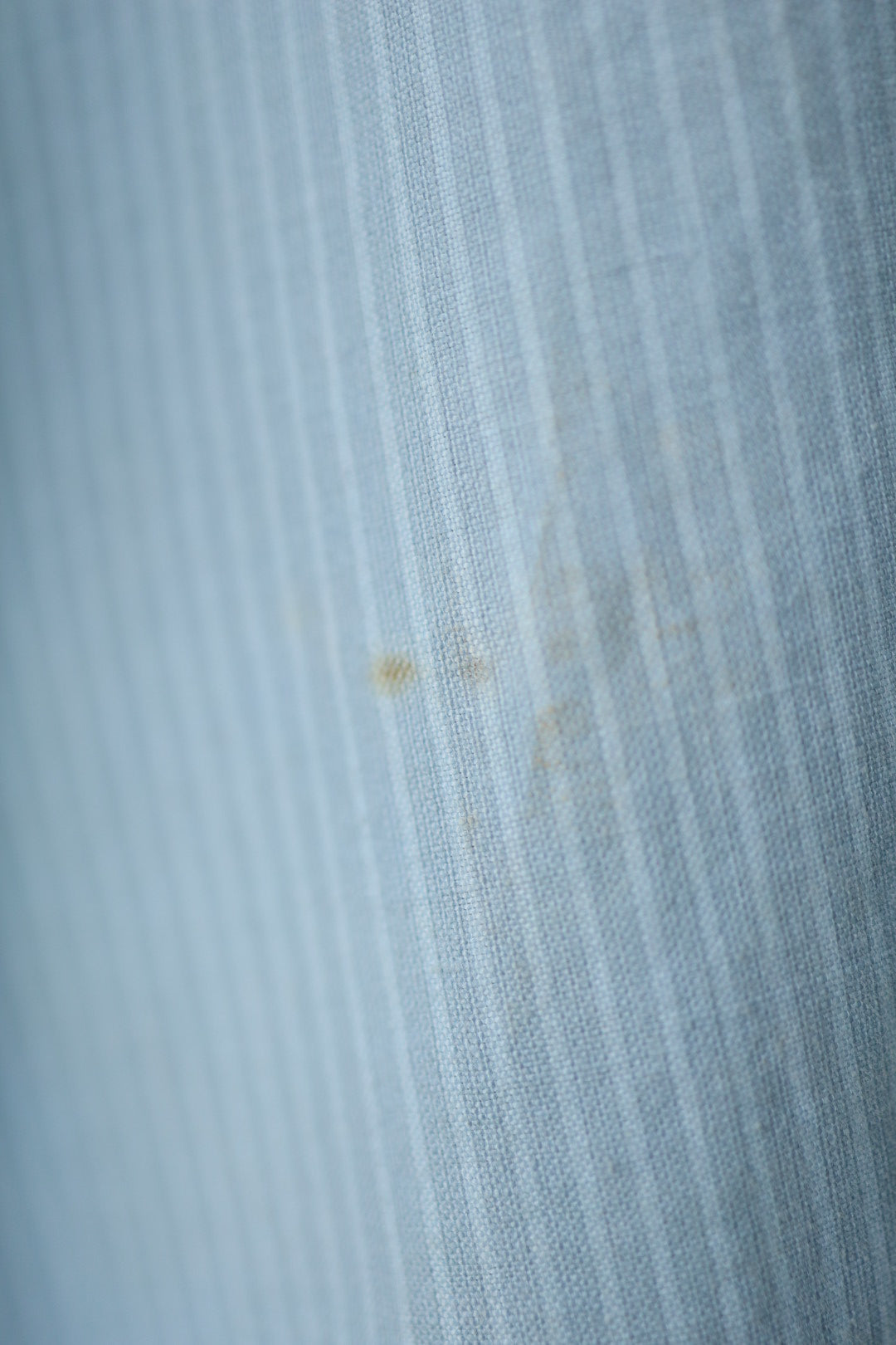 Close-up of a light stain on the front of the shirt, showing faded vertical stripes in the fabric.